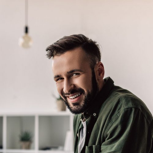 bearded businessman in casual clothing smiling at camera in modern office