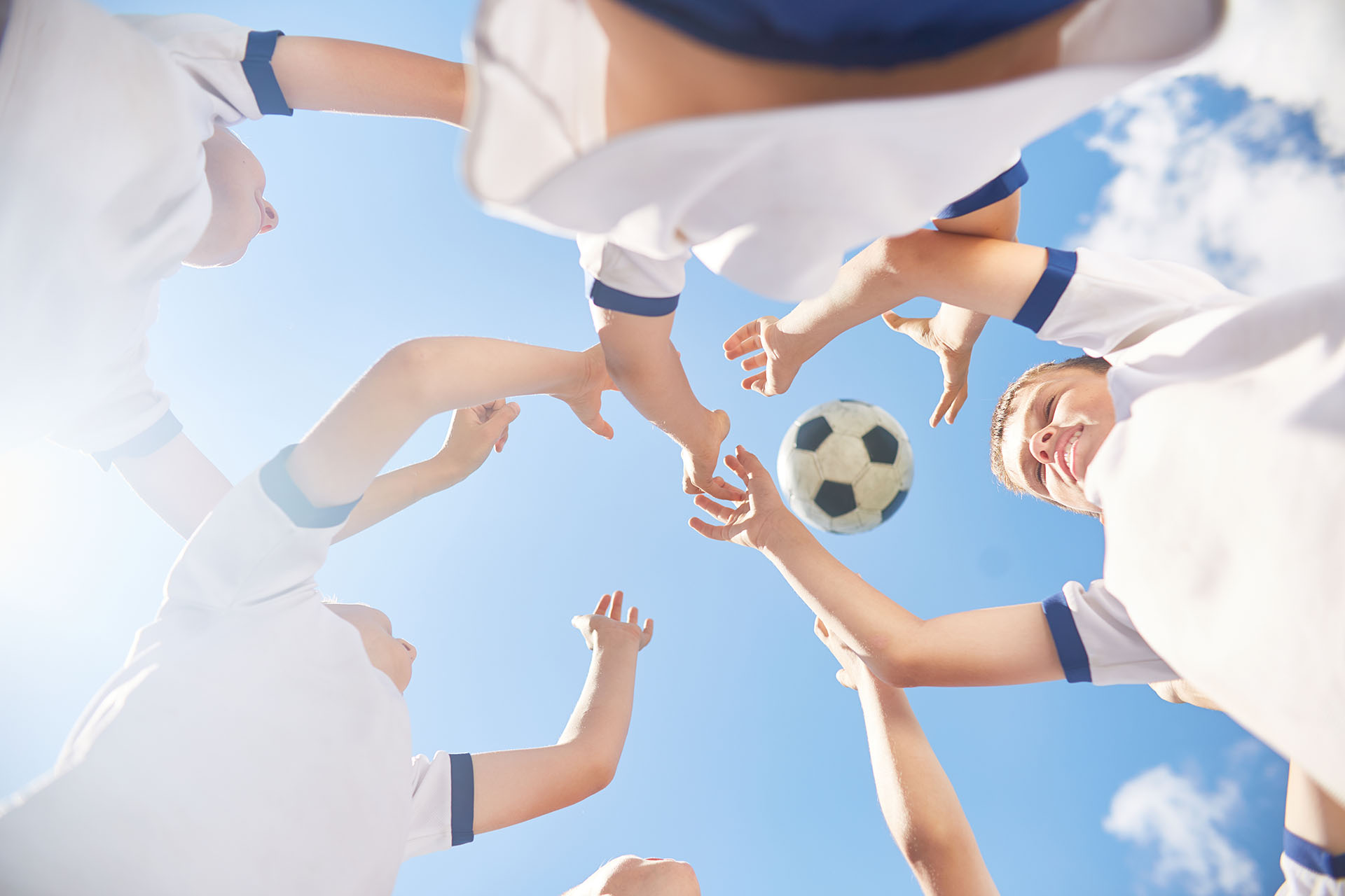Low angle view of boys in junior football team jumping trying to catch ball against clear blue sky